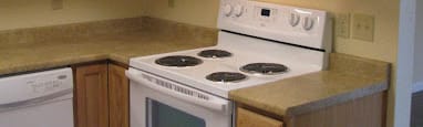 a kitchen with a stove and a microwave and wooden cabinets at Conifer Woods Apartments, Homer, AK