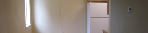 an empty room with a white refrigerator in it at Conifer Woods Apartments, Homer, Alaska
