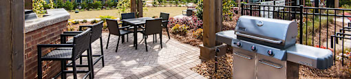 A wooden pergola over a patio with a grill and chairs.