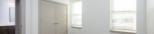A room with a carpeted floor, two closet doors, and a window with blinds.