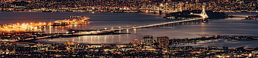 Cityscape at dusk with a bridge and a large ship in the water.