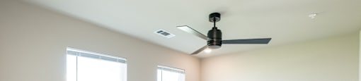 A room with a ceiling fan and two windows.