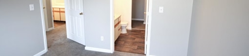 Empty bedroom with a white door and gray walls at Canterbury House apartments in Monticello, Indiana