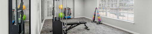 A spacious gym with a variety of equipment including a treadmill, a stationary bike, a rowing machine, and a weight bench.