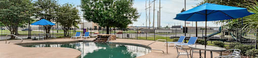 A pool area with a table and chairs and a blue umbrella.