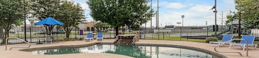 A pool surrounded by a fence with trees and chairs around it.