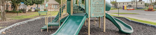 A playground with a green slide and a wooden structure.