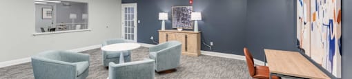 A room with grey walls and a grey carpet with a desk and chairs.