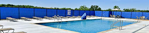 A pool surrounded by a blue fence with sun loungers on the side.