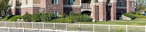 A large apartment building with a white picket fence in front.