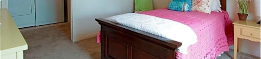 A bedroom with a pink bedspread and a wooden bed.
