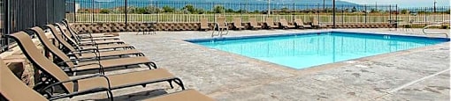 A pool surrounded by chairs and a fence.