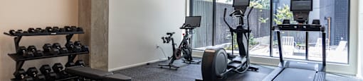a gym with weights and cardio equipment in a room with large windows at Analog PDX Apartments, Portland, OR 97227