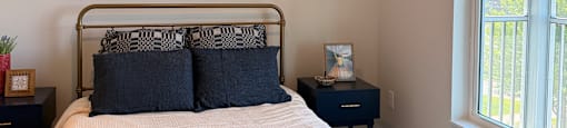 A bed with a white blanket and blue pillows is in a room with a ceiling fan.