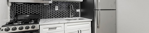 A kitchen with a black refrigerator, white cabinets, and a black and white tiled backsplash at 1355 Pearl in Denver, CO