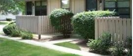 A house with a white fence and green bushes in front.