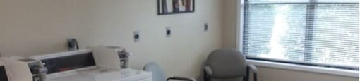 A laundry room with a washer and dryer, a chair, and a window.