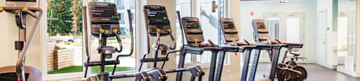 a gym with various cardio machines and a large window