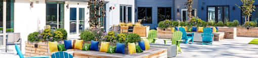 an outdoor patio with blue chairs and benches in front of an apartment building
