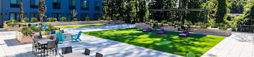 a patio with tables and chairs next to a lawn and a blue building