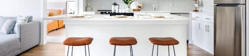 a white kitchen with three stools in front of a counter