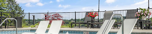 A pool with a white fountain in the middle and two white loungers.