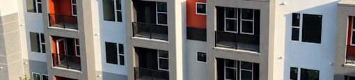 A modern apartment building with balconies and trees in front.