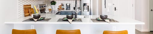 a white kitchen with orange chairs and a counter