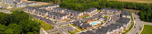 Overhead view of apartment buildings, clubhouse and pool; community is surrounded by trees and grass