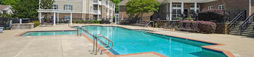 A large swimming pool surrounded by a concrete patio and a building in the background.
