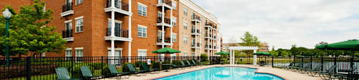 Pool with chairs and umbrellas next to apartment building and pond