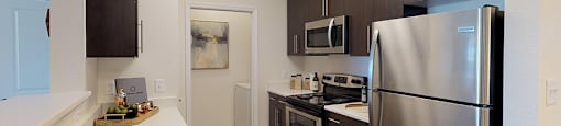 Kitchen with dark cabinets, granite countertops, vinyl wood plank floors; open to living room; laundry room with washer and dryer
