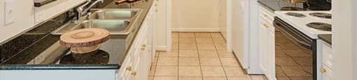 Galley kitchen with white cabinets, tile floors, granite countertops; laundry room