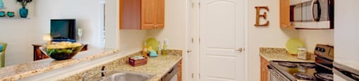 Galley-style kitchen with upgraded granite countertops and stainless steel appliances; door to washer/dryer room; open to living room