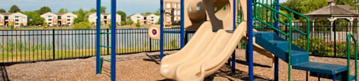 Playground with slide, monkey bars and steps; surrounded by a fence; overlooking community lake