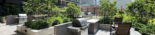 A rooftop patio with a grill and chairs overlooking a city skyline.