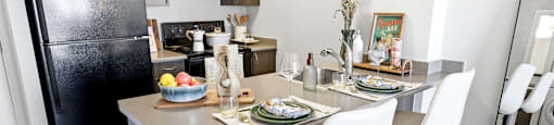 A kitchen with a black fridge, a table with chairs and a vase of flowers.