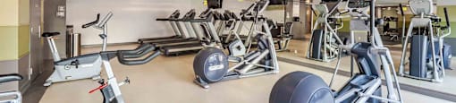 A gym with a variety of exercise equipment including treadmills, stationary bikes, and weight machines.