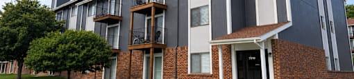 A modern two-story apartment building with a brick facade and a balcony on the second floor.