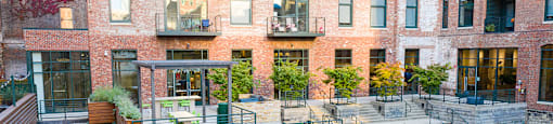 A courtyard surrounded by brick buildings with a bench and a tree.
