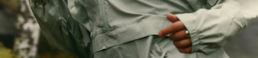 A person in a green jacket and brown shorts is running.