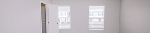 A room with a carpeted floor and two windows with blinds.