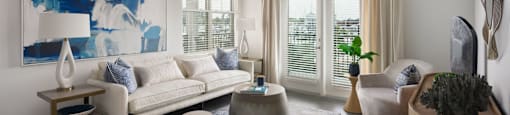 A living room with a white couch, a blue abstract painting, a wooden coffee table, and a rug at The Port at East Beach Apartments and Marina in Norfolk, 23518