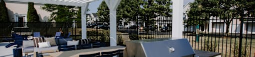A white pergola is over a stone and metal grill.
