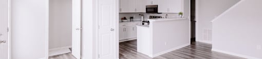 A spacious kitchen with white cabinets and a light wood floor.