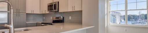 a kitchen with white cabinets and a large window at The Port at East Beach Apartments and Marina, Virginia, 23518