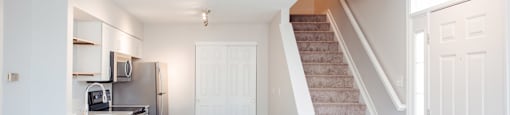 A kitchen with a refrigerator, microwave, and oven is adjacent to a staircase.