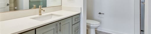 a bathroom with a sink, toilet, and mirror at The Port at East Beach Apartments and Marina, Norkfolk