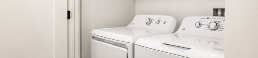 a washer and dryer in a white laundry room with a shelf above it