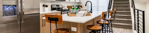a kitchen with a counter with bar stools and a stainless steel refrigerator